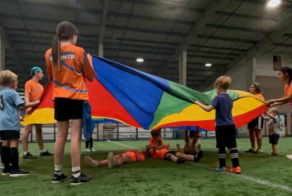 Children and adults playing with a parachute, participating in a daytime PE class at Bremerton Sports Center