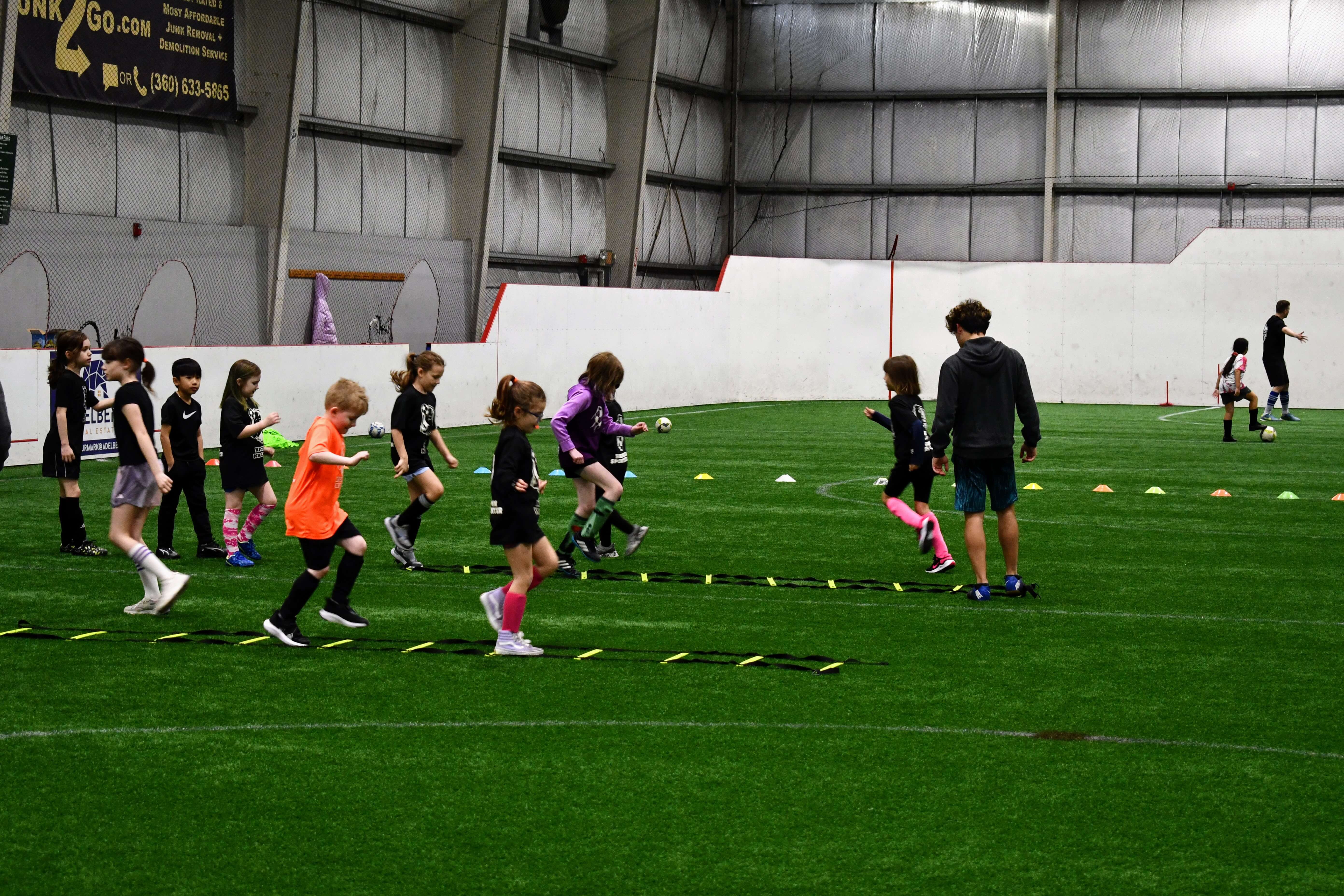 Children running a couple ladders on the ground with instructors at Bremerton Sports Center